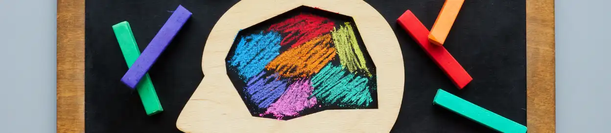 A wooden outline of a human head, with space in the middle filled with multi-coloured chalk scratchings (to illustrate neurodivergence)
