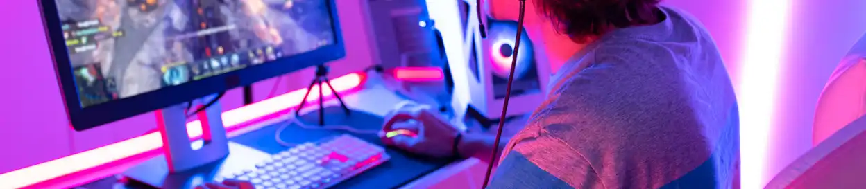 A young man in room backlit with pink argon lights plays a MMORPG on his desktop computer