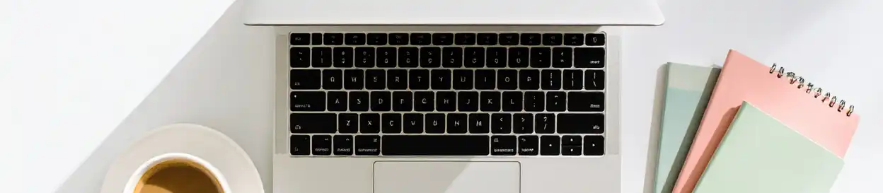 A laptop computer, three notepads, and a cup of coffee on a saucer