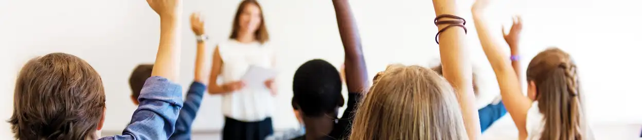 a teacher leads a class, several students' arms are raised