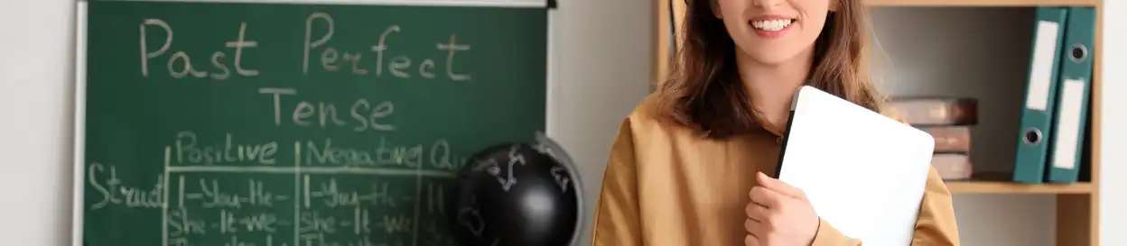 A teacher stands in front of a board, with Past Perfect Tense written on it