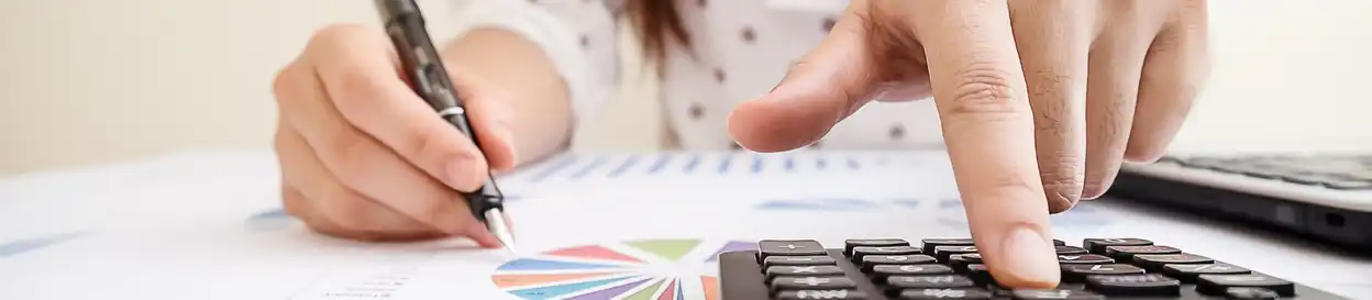 A pair of hands in the foreground, working on a calculator and a sheet of paper with a graph