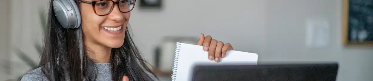 a young person conducts a lesson online. She is wearing headphones and holding a pad of paper.