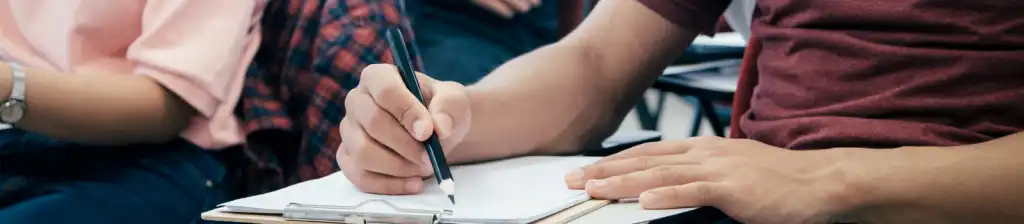 A young person writing down notes in a classroom