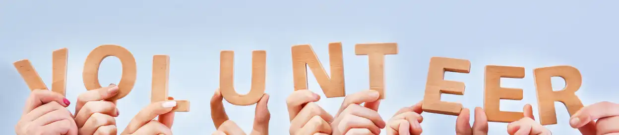 Many hands holding up letters spelling out "Volunteer"