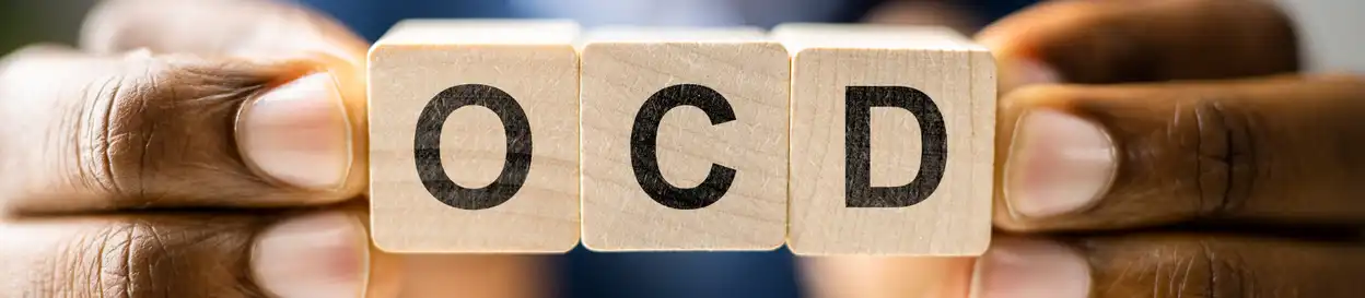 wooden blocks spelling out the letters "OCD", held between fingers