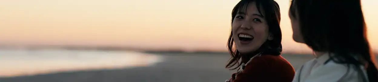 Two girls share a laugh on a beach, under the sunset