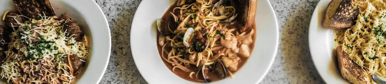 Three bowls of pasta including one with seafood