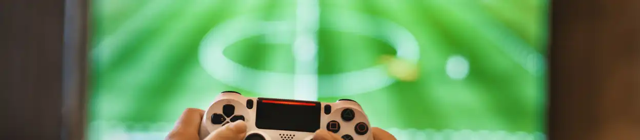 Someone holds a Playstation controller, playing a football (soccer) video game