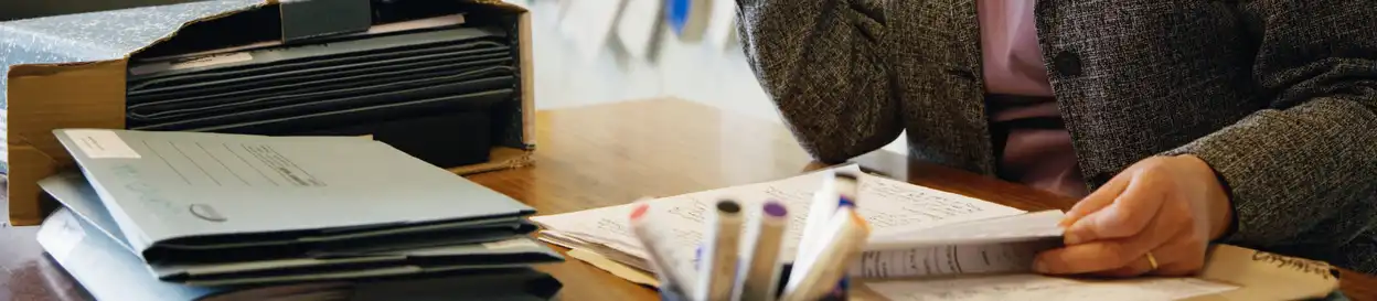 Pens on a desk, as a teacher works on sheets of paper