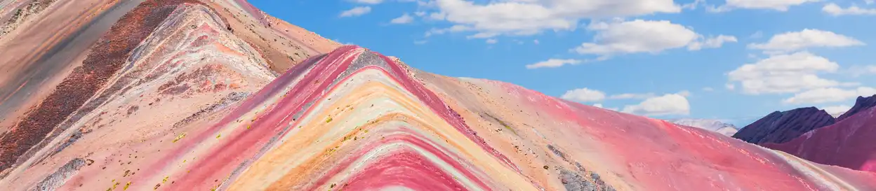 A colourful hill in Vinicunca, Peru. Shades of pink, yellow, orange, white and blue can be seen on the rock.