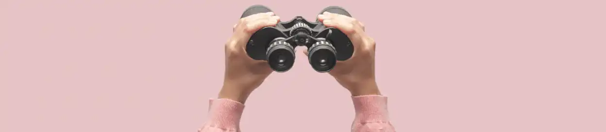 A pair of binoculars held up against a pink background