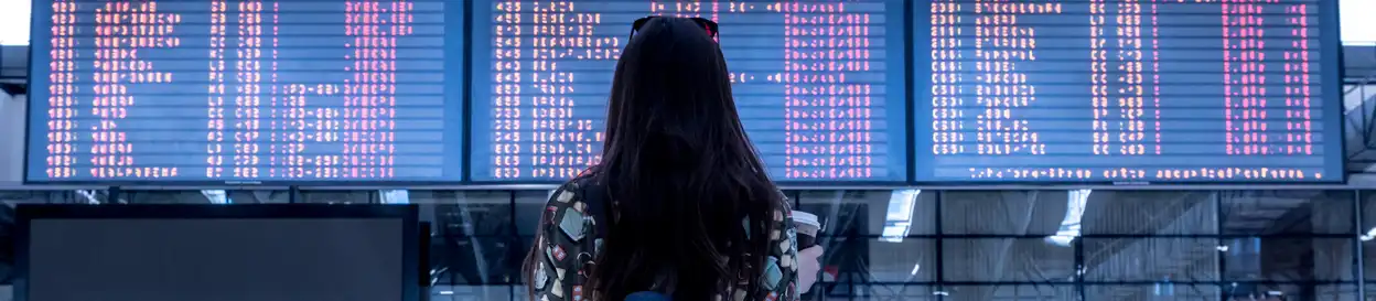 A woman standing in front of an airport departure board