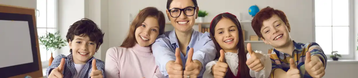 A teacher and her students smiling and holding their thumbs up 