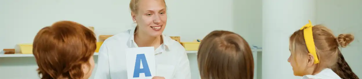 A teacher holding up the letter 'A' printed on a piece of paper for her young students