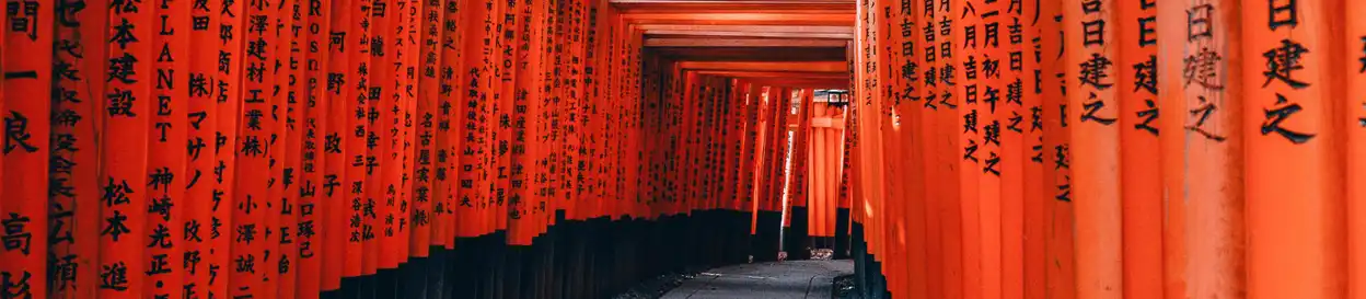 A walkway lined with red pillars with Japanese writing on them