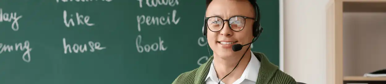 A man with a  headset sitting in front of a blackboard with English words written on it