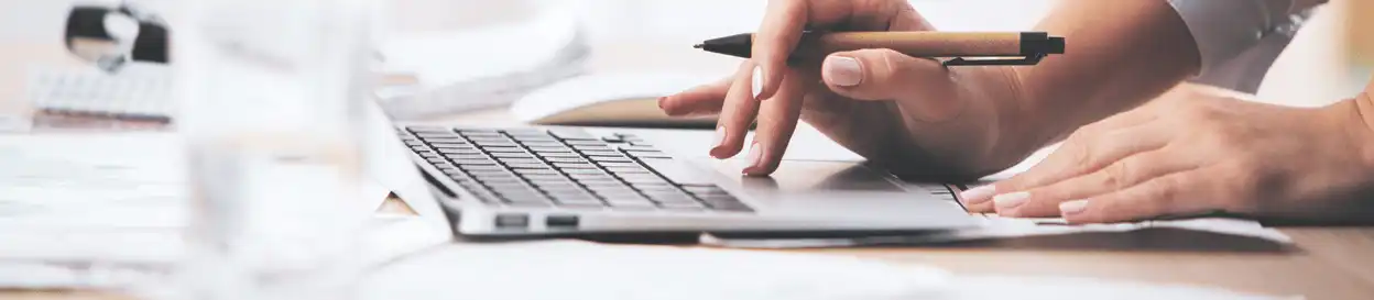 A woman holding a pen and typing on a laptop