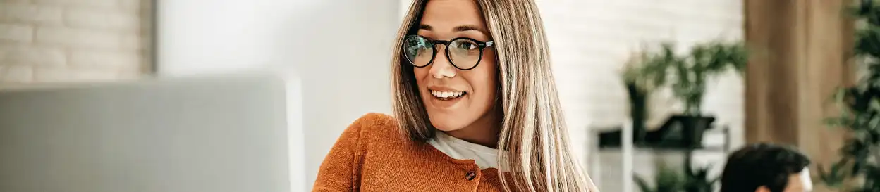 A woman with glasses smiling as she looks at her laptop