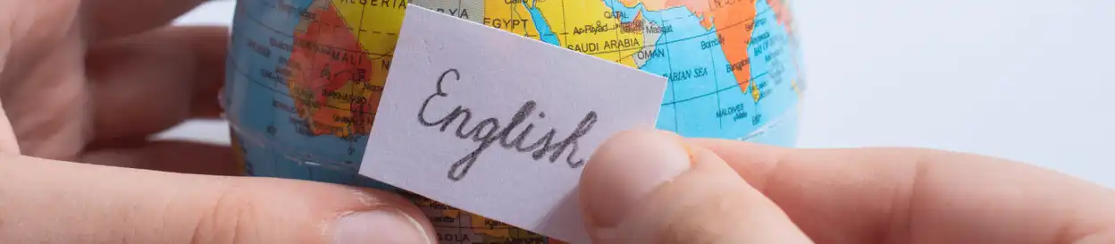 A person holding a small card with the word 'English' written on it in front of a small globe