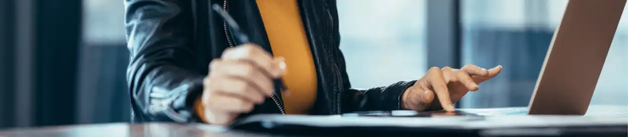 A woman in a leather jacket looking online and writing something in a notepad