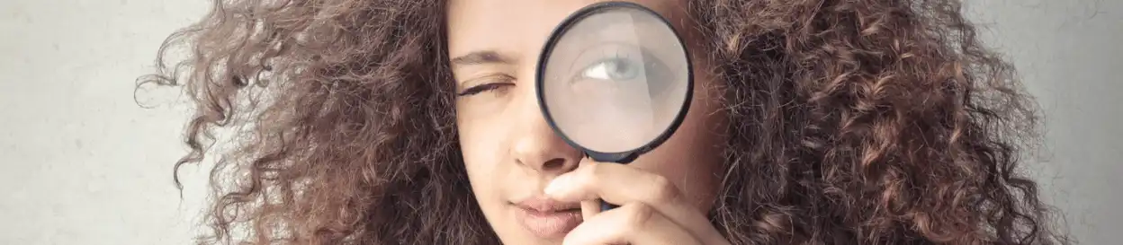 A woman holding up a magnifying glass to her eye