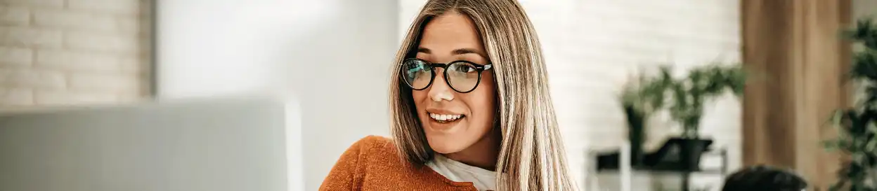 A woman wearing glasses and smiling as she looks at her laptop