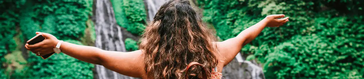 A woman with her arms outstretched in front of a waterfall