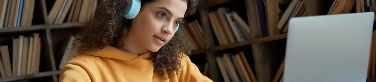 A young woman with blue headphones on sitting in front of a laptop